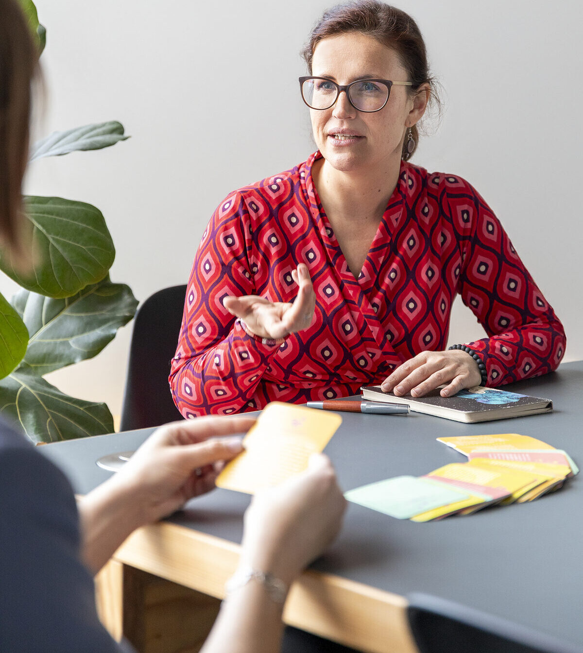 Coach Susanne an einem Tisch sitzend im Gespräch mit einer Klientin, vor sich farbige Karten und ein Notizheft während einem Coaching für Schulleitungen